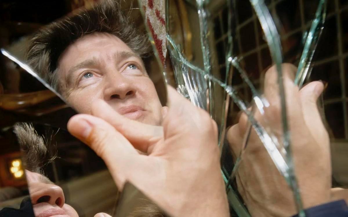 Титульное изображение для страницы события: кадр из фильма «Линч/Оз», рука держит осколок зеркала, в котором отражается Дэвид Линч