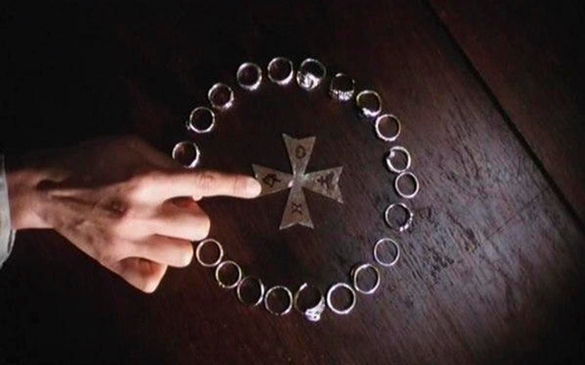 Титульное изображение для страницы события: кадр из фильма «Любовное сражение во сне»,  палец положен на конец металлического креста, лежащего на столе в окружении колец