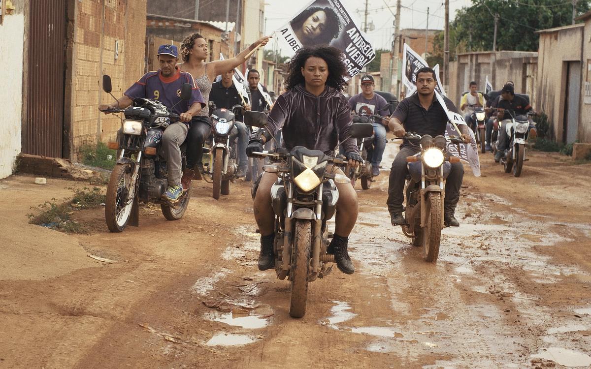 Титульное изображение для страницы события: кадр из фильма «Пустошь в огне»,  женщины с знаменами в руках едут на мотоциклах по грязной городской улице