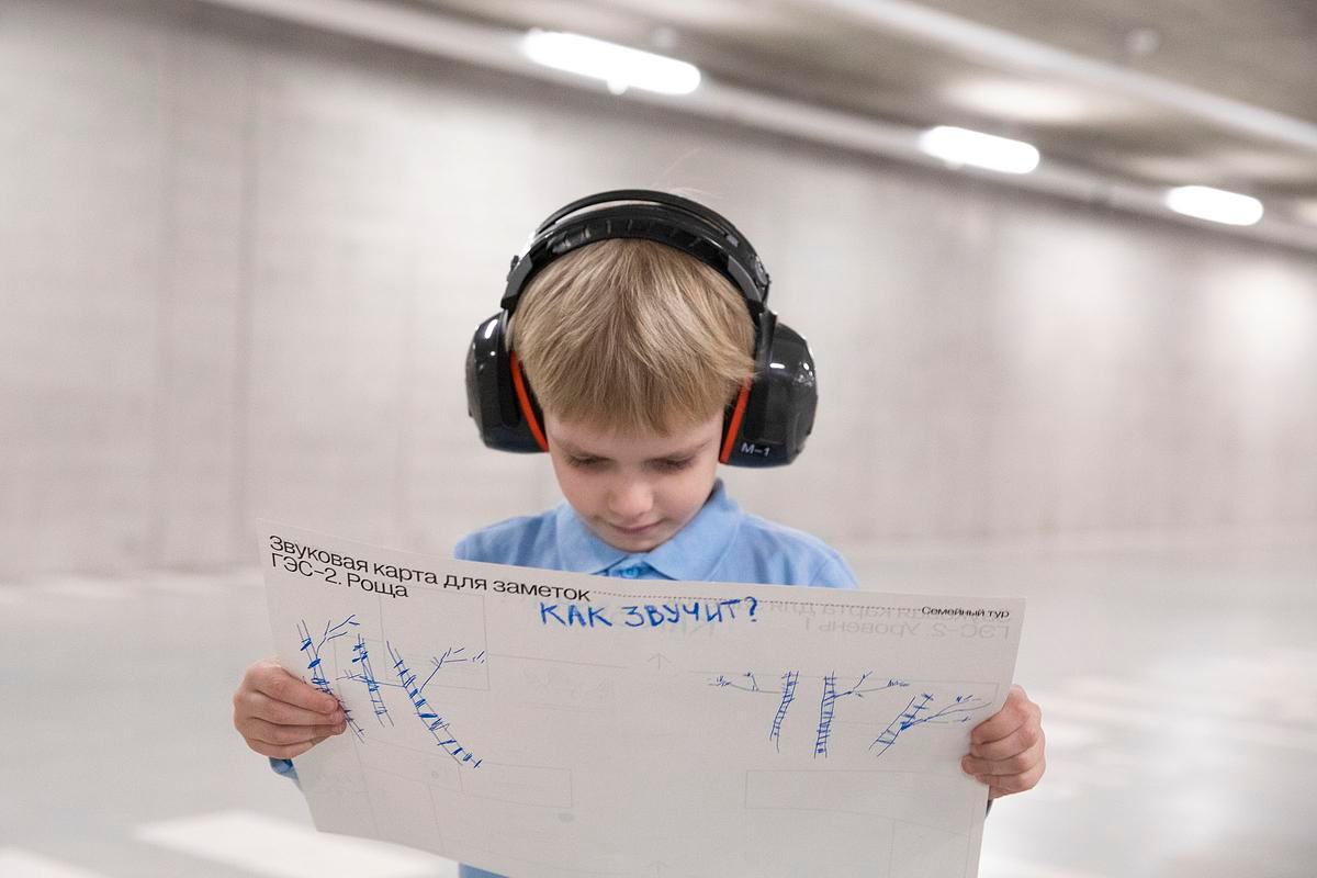 Титульное изображение для страницы события. Фото: мальчик в наушниках держит в руках и изучает «Звуковую карту для заметок» – большой белый лист с печатным текстом и рисунками от руки 