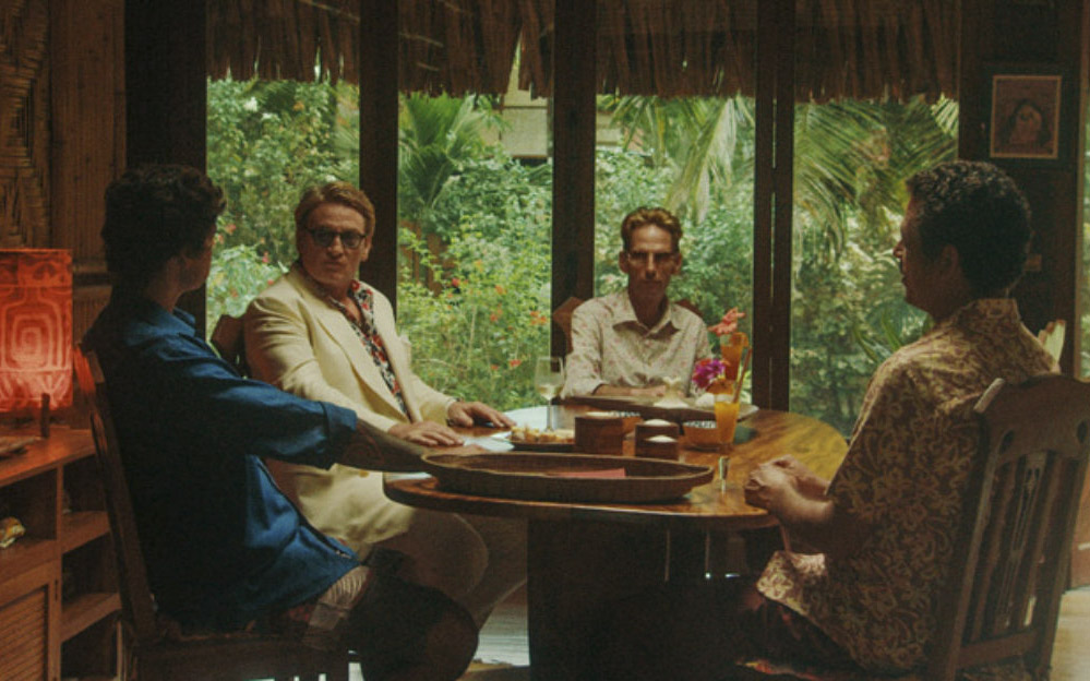 Четыре мужчины сидят за круглым столом, за окном джунгли