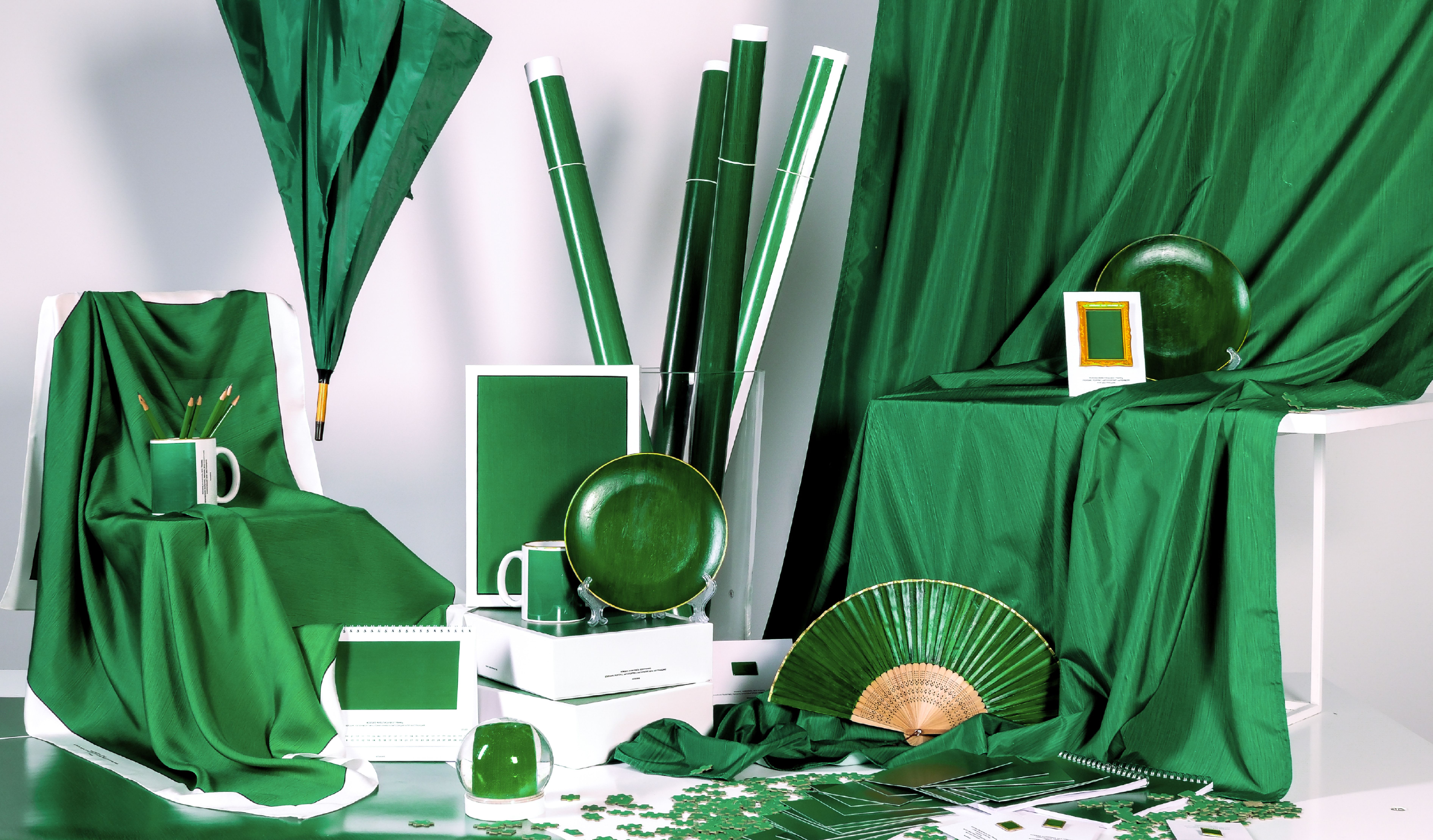 Изображение. Постановочное фото — на фоне драпировки из зеленой ткани расставлены предметы: чашки, карандаши, веер, рамка для фотографий, стеклянный шар, тарелки. Все выдержано в зелено-бело-золотой цветовой гамме