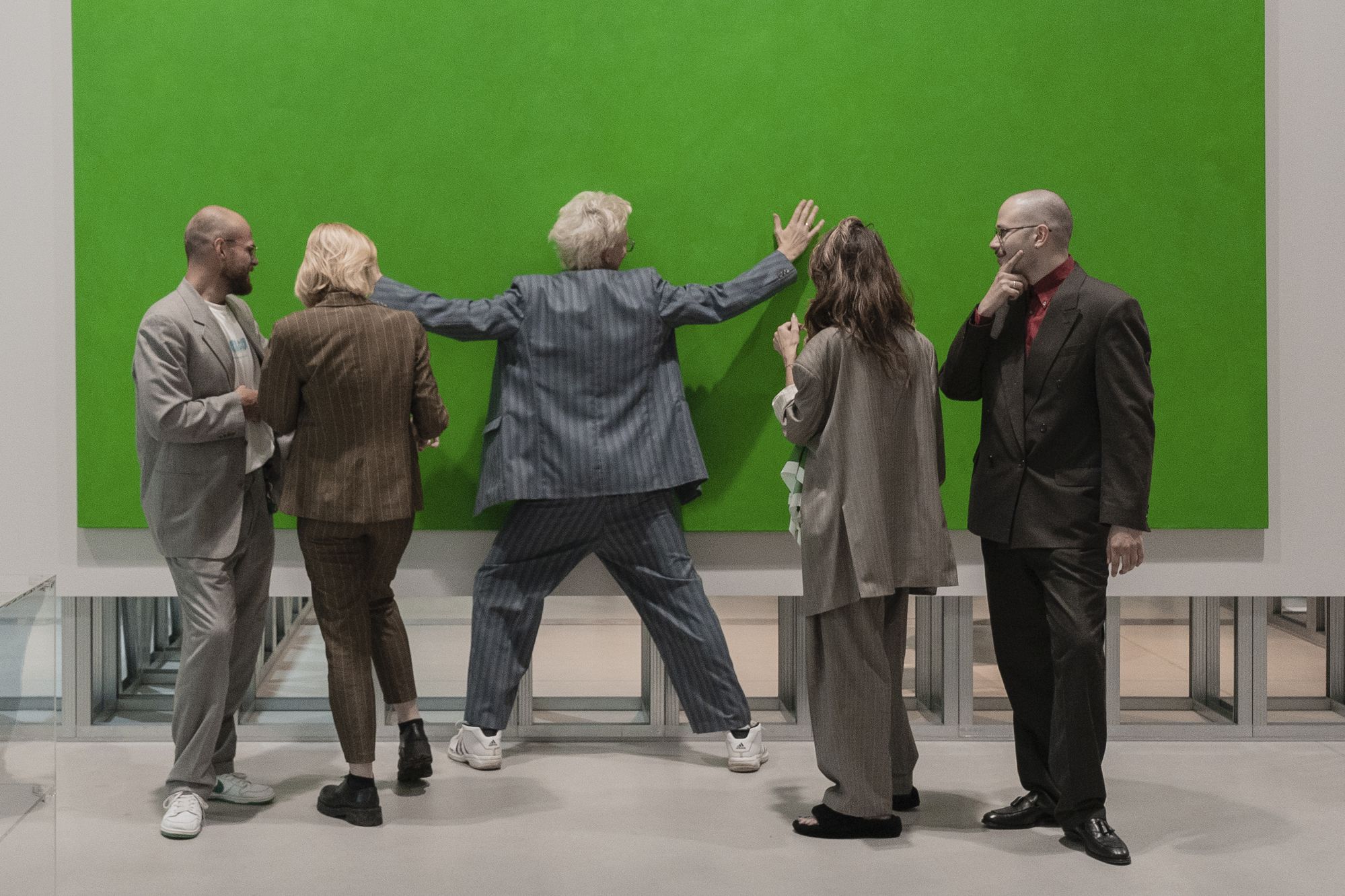 5 человек в костюмах стоят напротив зеленого прямоугольника, один расставил перед ним руки
