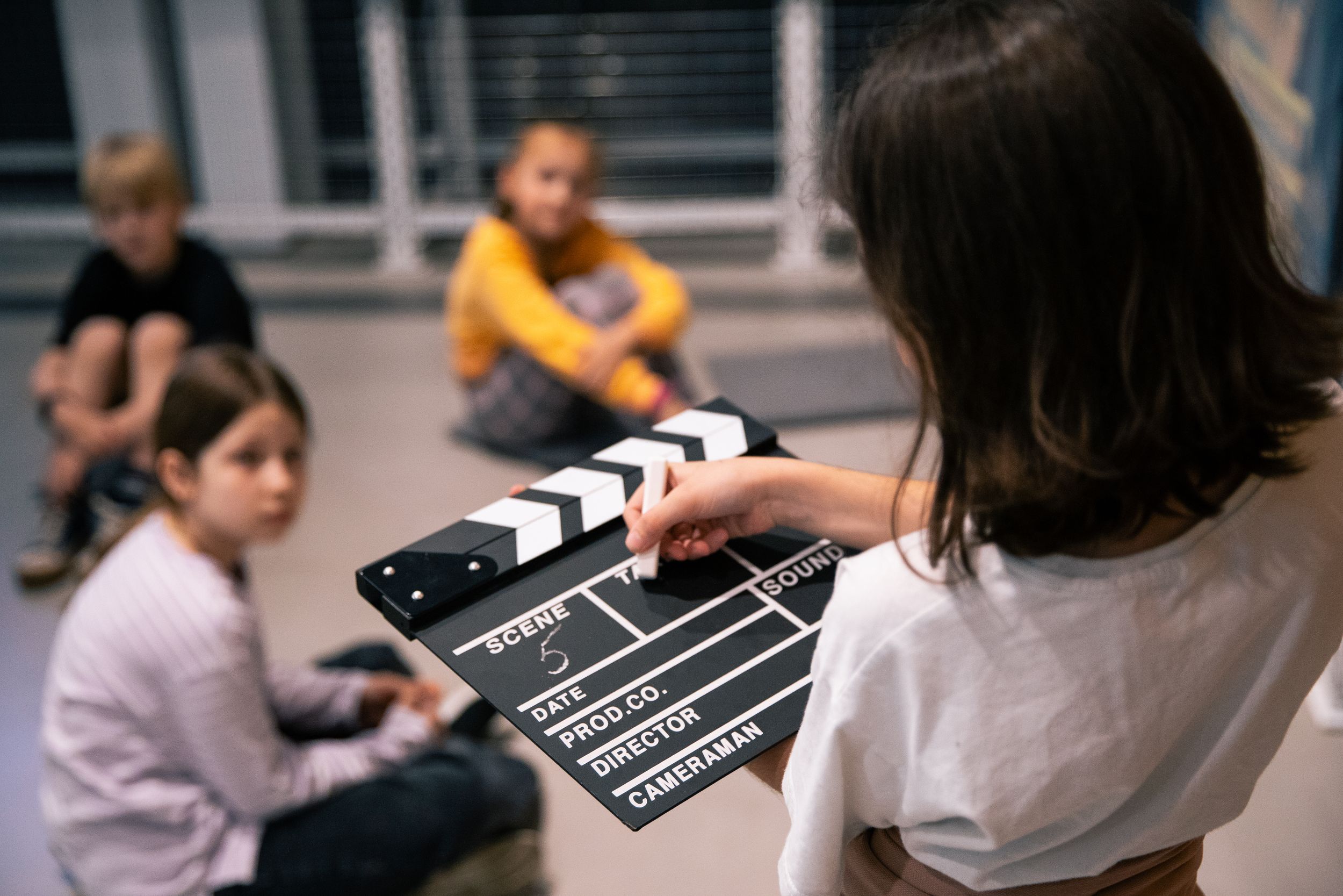 Девочка пишет на кинохлопушке, на фоне сидят трое детей