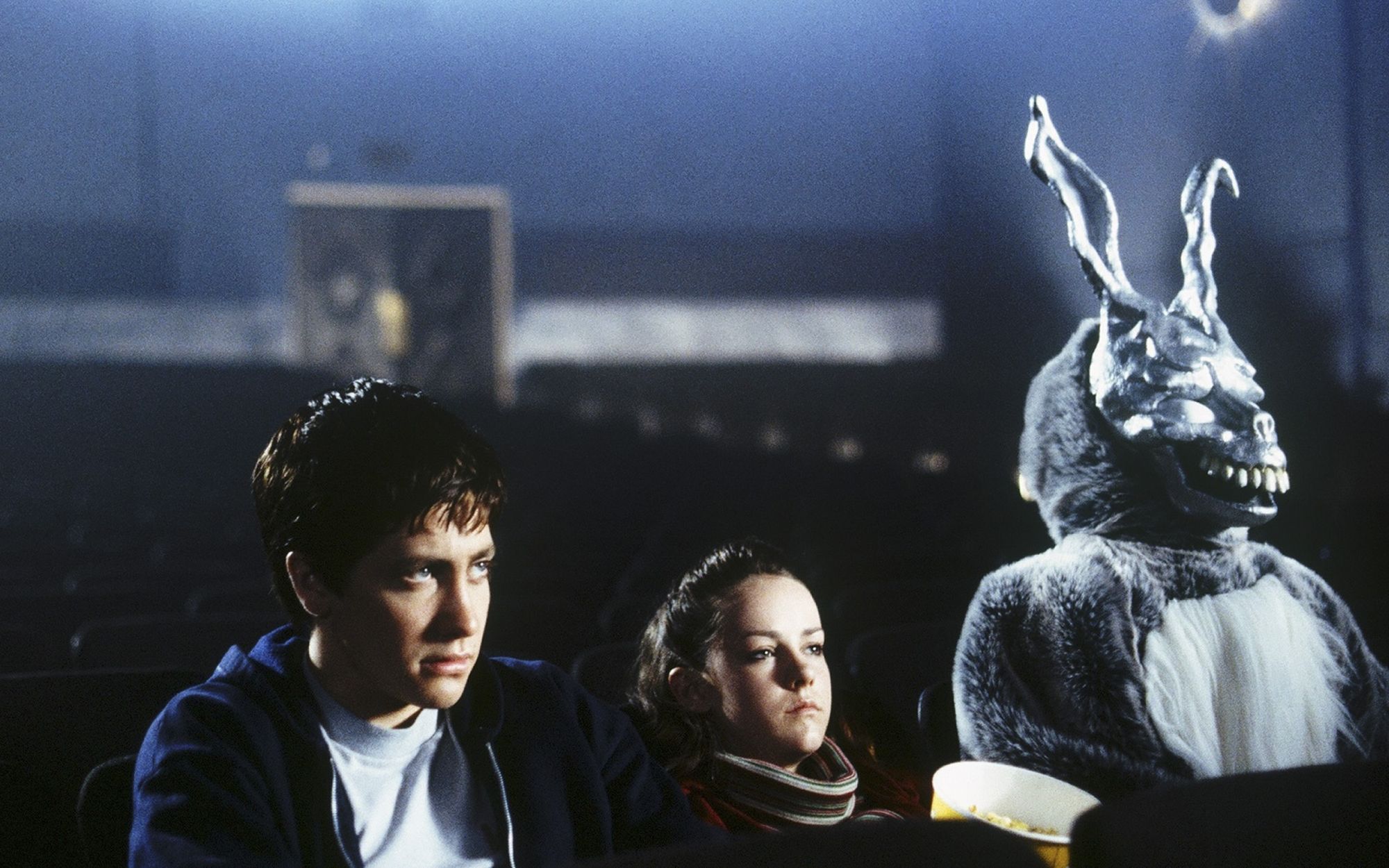 В зале кинотеатра сидят парень, девушка и человек в костюме кролика и маске скелета