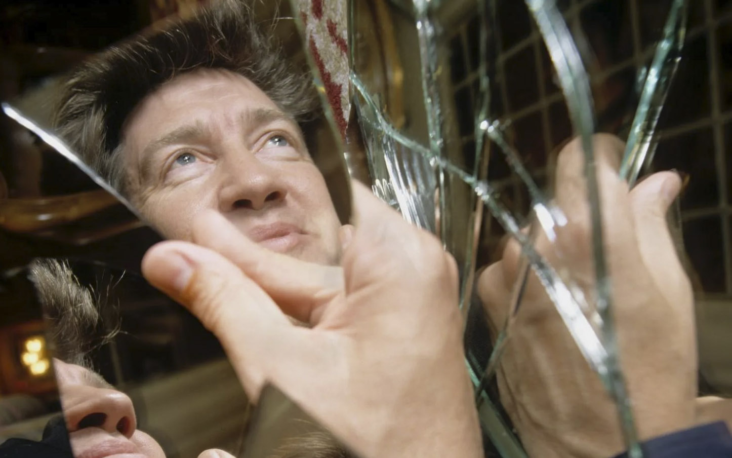 Рука держит осколок зеркала, в котором отражается Дэвид Линч