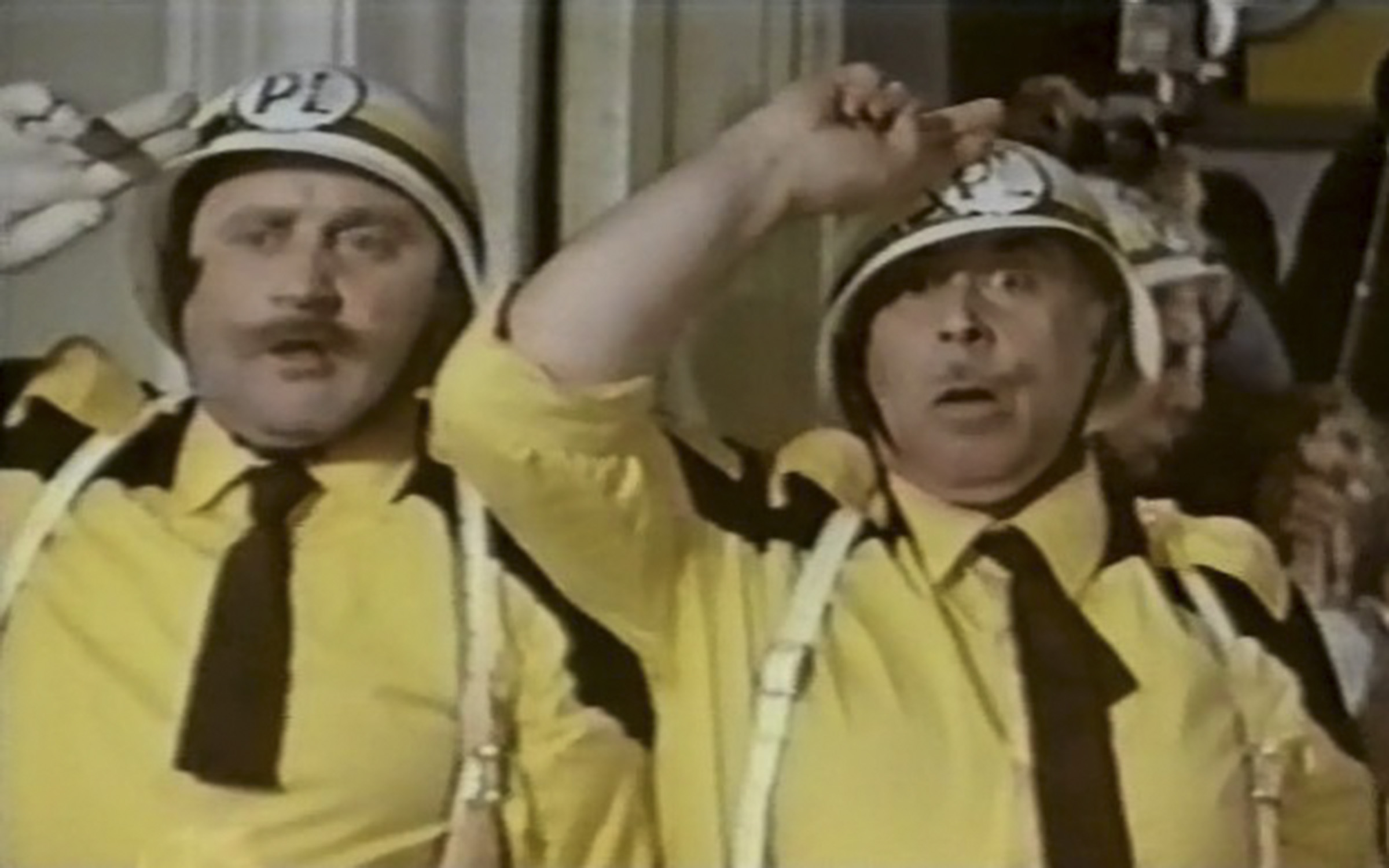 Два мужчины в желтых рубашках, черных галстуках и касках отдают честь