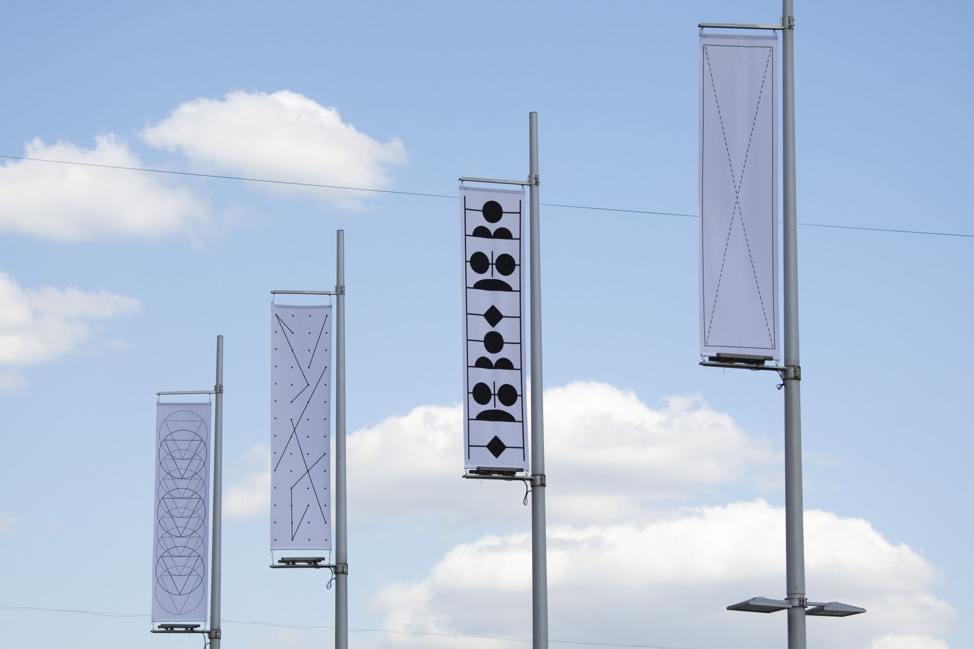 Флагштоки с вертикальными прямоугольными знаменами с фирстилем выставок <nobr>ГЭС-2</nobr> на фоне голубого неба