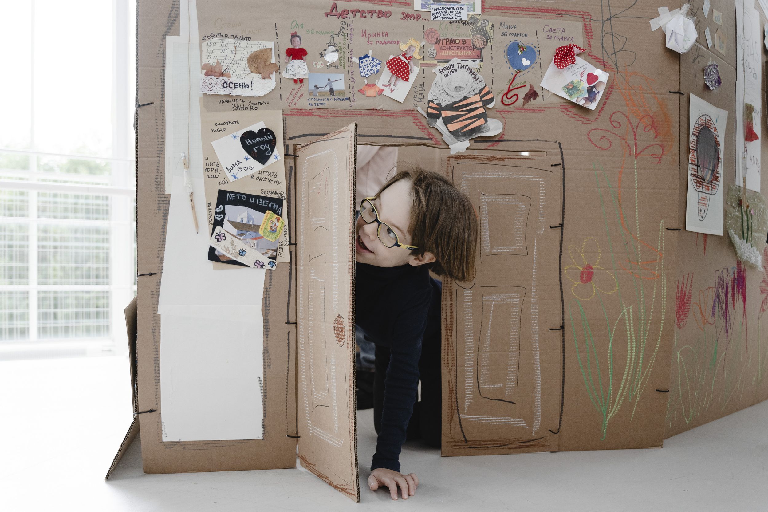 Ребенок в очках выглядывает из двери, сделанной в коробке