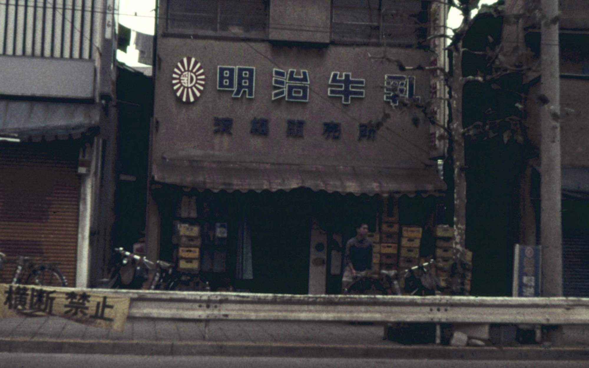 Человек сидит у входа в задние с японскими надписями на фасаде