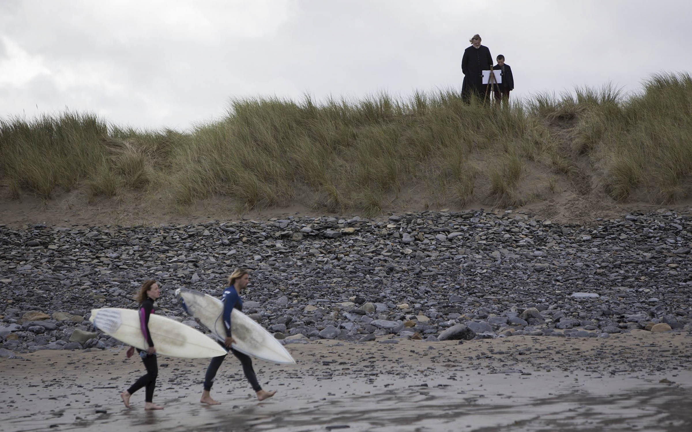 Кадр из фильма «Голгофа», два серфера идут по ирландскому пляжу