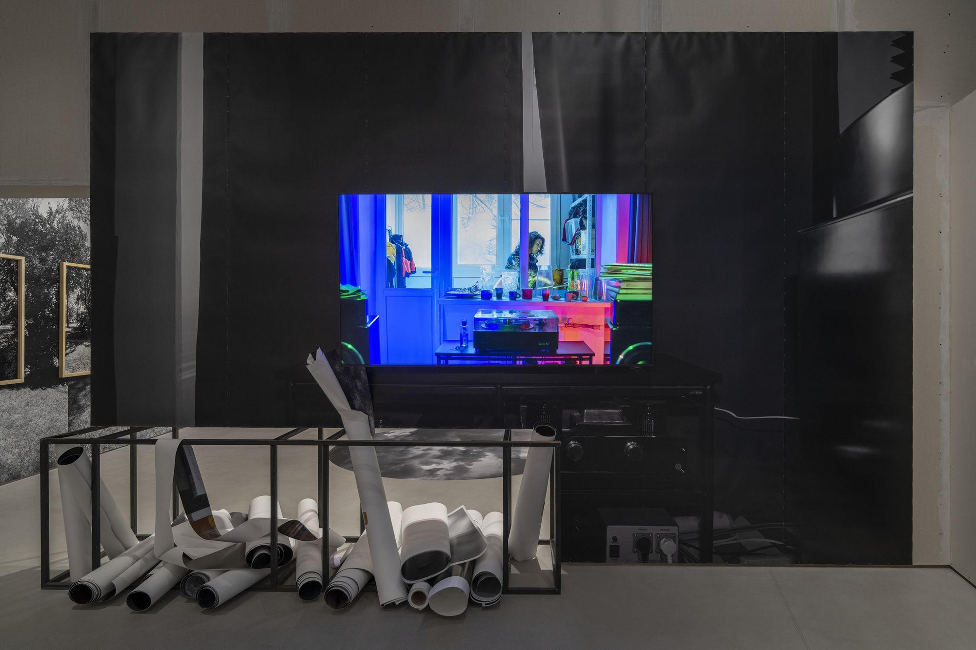 Экспонат, телевизор с видеоартом, снизу лежат большие рулоны бумаги