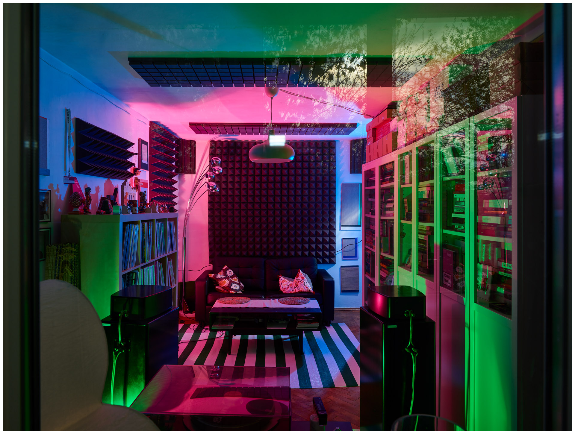 Фотография интерьера квартиры, диван под окном, окно завешано звукоизоляционным материалом, освещение зелено-розовым светом