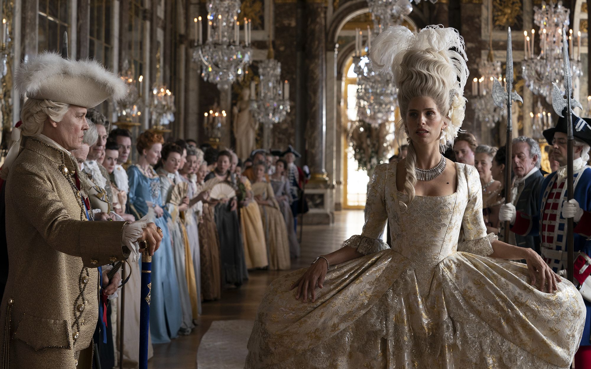 Женщина в платье с кринолином и перьями в волосах идет под дворцу вдоль ряда пышно одетых слуг