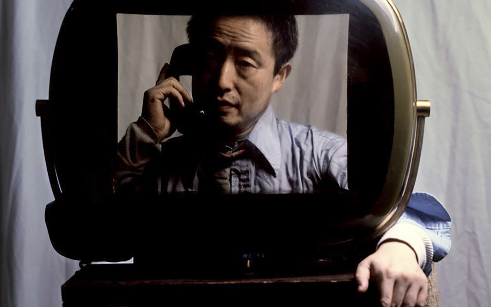 Мужчина с телефонной трубкой у уха сидит в раме в виде экрана телевизора