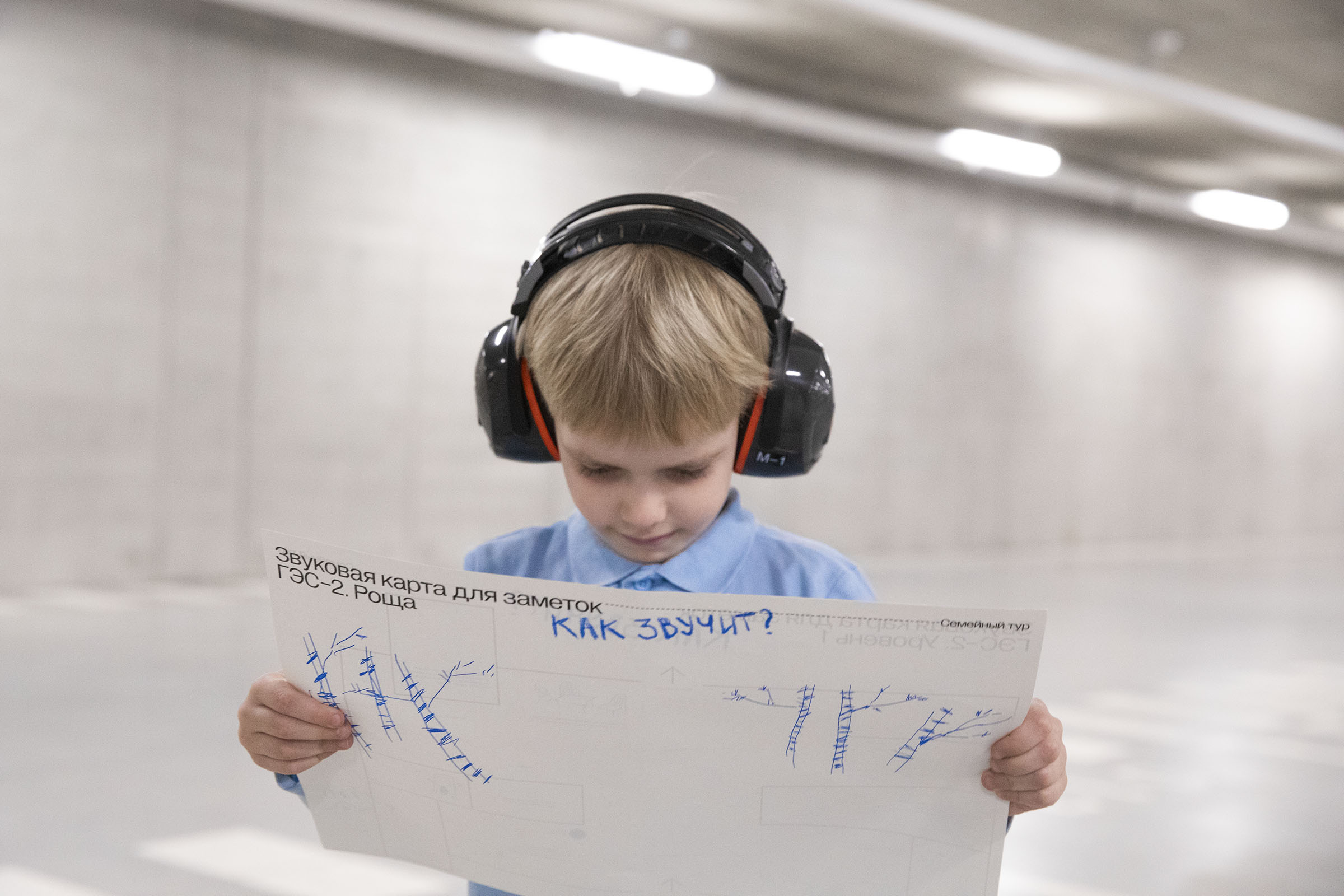 Фото: мальчик в наушниках держит в руках и изучает «Звуковую карту для заметок» – большой белый лист с печатным текстом и рисунками от руки 