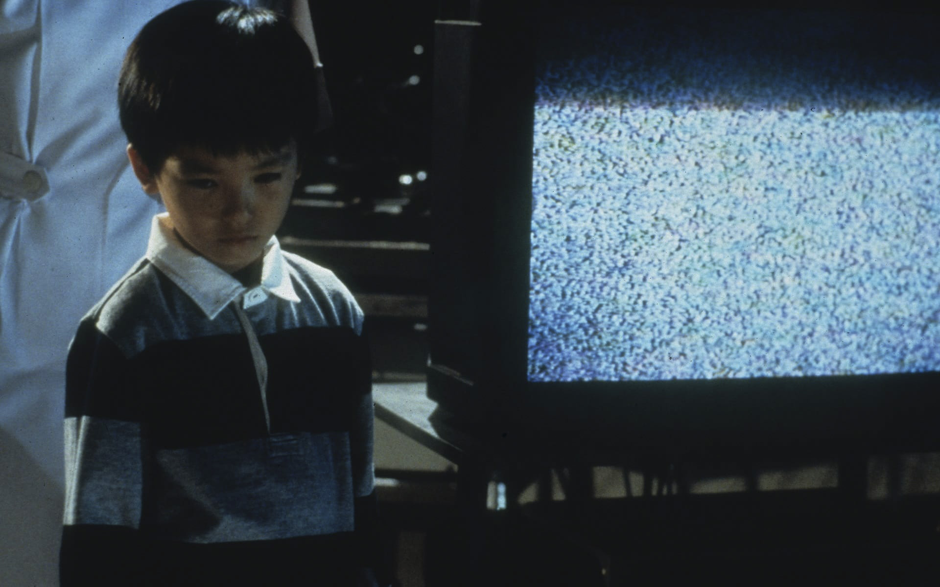 Мальчик стоит около телевизора с включенным белым шумом и смотрит в сторону